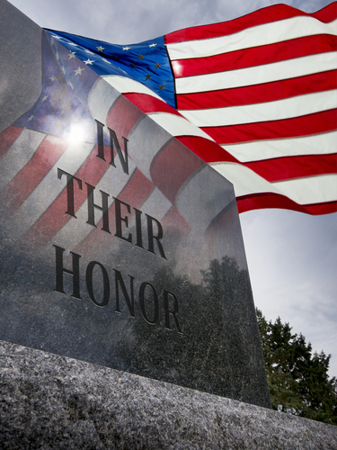 Flag waving over stone etched with the words: "In Their Honor"